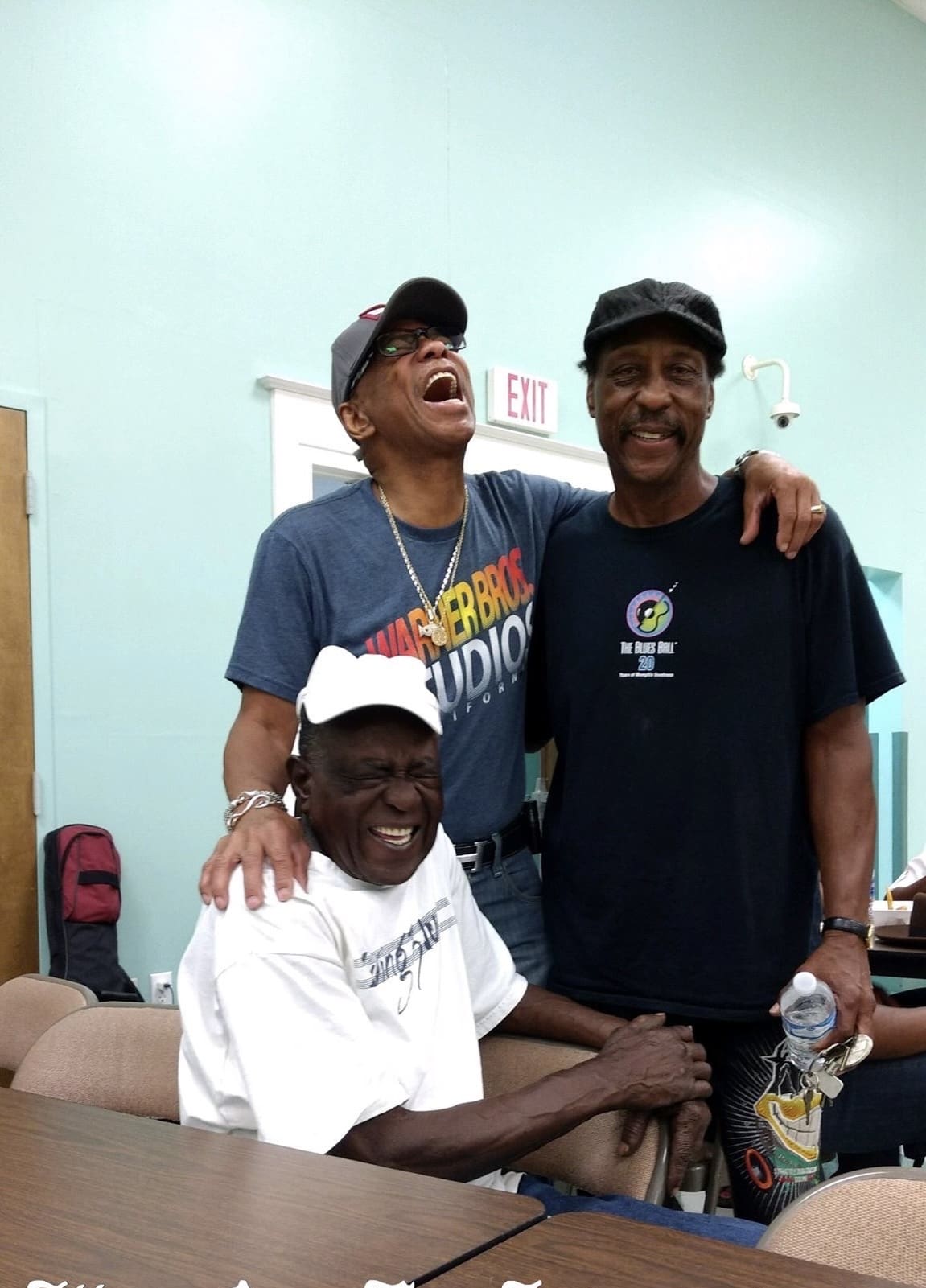 Three men pose for a picture in front of a wall.